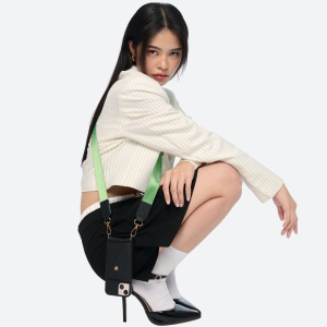 Model wearing the black Bandolier-style leather crossbody phone case, demonstrating its practicality with the adjustable strap comfortably slung over the shoulder.